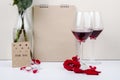 side view of red roses in a glass bottle standing near a sketchbook and two glasses of red wine on white background Royalty Free Stock Photo