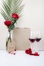 side view of red roses with palm leaf in a glass bottle standing near a sketchbook and two glasses of red wine on white background Royalty Free Stock Photo