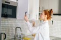 Side view of redhead young woman opening door of kitchen cabinet at light modern kitchen room. Royalty Free Stock Photo