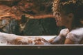 Side view of relaxed african american naked young woman taking bath at home, laying in beautiful bathtub, rubbing her skin with Royalty Free Stock Photo