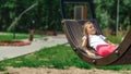 Side view of relaxed pensive little girl in casual clothes lying on a swing and spending a sunny summer day in the park. Girl is Royalty Free Stock Photo