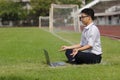 Side view of relaxed young Asian business man with laptop doing yoga position on the green grass of stadium. Royalty Free Stock Photo