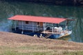 Side view of river barge converted into river boat house with improvised homemade roof left at local river bank