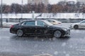 Side view rolling shot with black car in motion during snowfall. Mercedes-Benz Maybach S560 driving along winter city street with