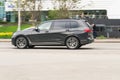 Side view rolling shot with gray SUV car in motion. BMW X7 G07 driving along the street in city with blurred background