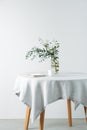 Side view round table with a rough white tablecloth and branch in a jar