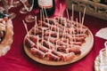 Side view of a round wooden plate with sliced and twisted pieces of meat on skewers. Catering