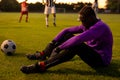 Side view of sad african american male goalkeeper sitting on field at playground during sunset Royalty Free Stock Photo