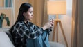 Side view of sad bored Asian woman girl sitting on sofa at home with telephone serious unhappy lady scrolling browsing Royalty Free Stock Photo