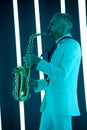 Side view saxophone player in a white suit against the backdrop of neon lamps with blue backlight. Saxophonist jazzman
