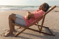 Side view of senior biracial man with laptop sleeping on folding chair relaxing at beach Royalty Free Stock Photo