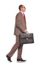 Side view of a senior businessman holding suitcase and walking Royalty Free Stock Photo