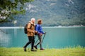 A side view of senior pensioner couple hiking by lake in nature.