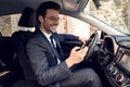 Side view of serious business man in suit using phone while sitting at the wheel in car Royalty Free Stock Photo