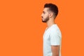 Side view of serious handsome brunette man looking left, empty copy space for text. indoor studio shot isolated on orange