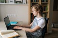 Side view of serious little Caucasian girl using laptop, typing, studying online at home sitting at desk with books by Royalty Free Stock Photo