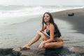 Side view of girl in bikini spends time on black sand beach. Young woman with long hair posing outdoor Royalty Free Stock Photo