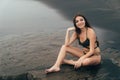 Side view of girl in bikini spends time on black sand beach. Young woman with long hair posing outdoor Royalty Free Stock Photo