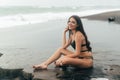 Side view of sexy girl in bikini spends time on black sand beach. Young woman with long hair posing outdoor Royalty Free Stock Photo