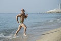 Side view of a sexy muscular man in colorful speedo running out of the sea. Professional male athlete getting out of the