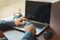 Side view shot of a man`s hands holding card and using laptop sitting at table in office with cup of black coffee. Royalty Free Stock Photo