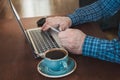 Side view shot of a man`s hands holding card and using laptop sitting at wooden table with cup of coffee. Close up. Royalty Free Stock Photo
