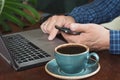 Side view shot of a man`s hands using smart phone and laptop sitting at wooden table. Close up. Royalty Free Stock Photo