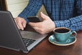 Side view shot of a man`s hands using smart phone and laptop sitting at wooden table with cup of black coffee. Close up. Royalty Free Stock Photo