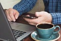 Side view shot of a man`s hands using smart phone and laptop sitting at wooden table with cup of coffee. Close up. Royalty Free Stock Photo