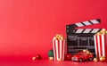 Side view shot of table adorned with popcorn boxes, festive baubles, miniature retro car, clapperboard against red wall background