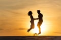 Side view of silhouettes of man and woman jumping on beach against sun Royalty Free Stock Photo