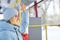 Woman wearing blue cap and jacket standing holding handle looking ahead in bus.