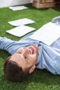 Side view of smiling businessman lying on grass with documents