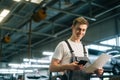 Side view of smiling handsome young mechanic male wearing uniform holding clipboard and using texting mobile phone