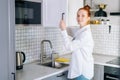 Side view of smiling redhead young woman opening door of kitchen cabinet at light kitchen room. Royalty Free Stock Photo