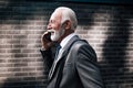 Smiling elderly entrepreneur talking on smart phone while walking by brick wall Royalty Free Stock Photo