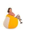Side view of smiling woman sitting on yellow beanbag chair isolated on white background Royalty Free Stock Photo