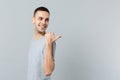 Side view of smiling young man in casual clothes looking back and pointing thumb aside isolated on grey wall background Royalty Free Stock Photo