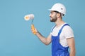 Side view of smiling young man in coveralls protective helmet hardhat hold paint roller isolated on blue background Royalty Free Stock Photo