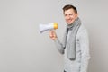 Side view of smiling young man in gray sweater scarf holding megaphone on grey background in studio. Healthy Royalty Free Stock Photo