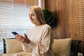 Side view of smiling young woman in casual clothes using smartphone at home, messaging or browsing social networks Royalty Free Stock Photo