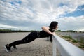 Side view of sports woman doing push ups on horizontal bar outdoors. Woman training near the stadium
