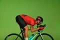 Side view of sportsman, cyclist on bicycle in sports uniform and protective helmet training isolated on green background
