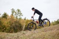 Side view of sporty man riding mountain bike on enduro track, guy dresses black track suit and cap, ridiing down hiil in forest, Royalty Free Stock Photo