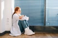 Side view of stressed upset female doctor feeling worried about professional malpractice sitting on floor near window in Royalty Free Stock Photo