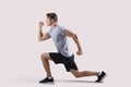 Side view of strong millennial guy in sportswear doing lunges on light studio background Royalty Free Stock Photo
