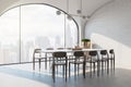 Side view on stylish dining table surrounded by wooden chairs on light floor in sunny room with brick wall and skyscrapers view