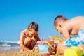 Side view of tanned preteen boy brother, little girl sister family sitting on beach near bucket, playing with sand. Royalty Free Stock Photo