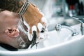 Side view of tattooed barber washing client hair before haircut in barbershop Royalty Free Stock Photo