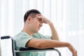 Side view, Teenage caucasian Male patient having stressed pose hand on head and sitting on wheelchair in hospital room.